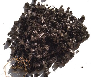May include: A close-up of a pile of black Himalayan salt crystals. The salt crystals are irregular in shape and have a dark, almost black color.