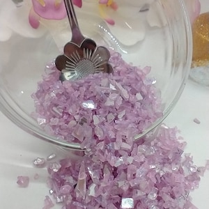 May include: A glass bowl filled with iridescent pink and silver glass glitter. The glitter is spilling out of the bowl onto a white surface.