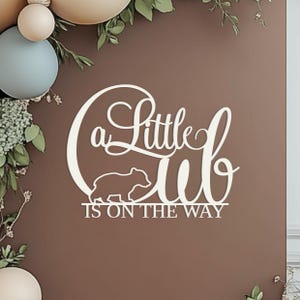 Un piccolo cucciolo è in arrivo, cartello per decorazioni murali sullo sfondo del baby shower, centrotavola per foto con tema bosco e orso in legno
