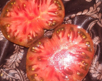 May include: Two halves of a red tomato with black skin and many seeds. The tomato is cut in half and the inside is visible.