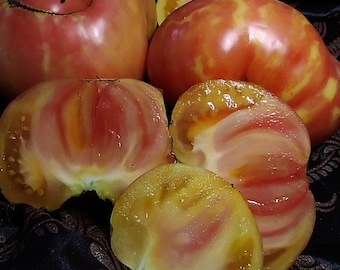 May include: Close-up of four heirloom tomatoes, two whole and two sliced. The tomatoes are a vibrant mix of red, yellow, and pink with a striped pattern. The flesh is a pale yellow with red streaks.