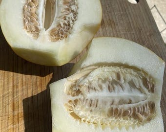 Puede incluir: Dos mitades de melón cantalupo sobre una tabla de cortar de madera. La pulpa de color amarillo pálido del melón es visible, junto con las semillas y la cáscara marrones. Las superficies cortadas muestran la estructura interna del melón.