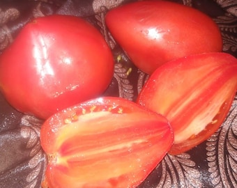 May include: Four red tomatoes, two whole and two halved, with visible seeds. The tomatoes are on a brown patterned fabric background.
