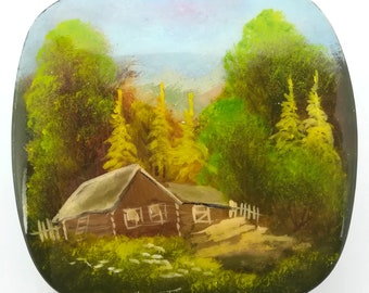 May include: A hand-painted, square-shaped decorative item featuring a landscape scene. The artwork depicts a wooden cabin nestled among lush green and yellow trees, with a white picket fence. The sky is a blend of blue and pink hues.