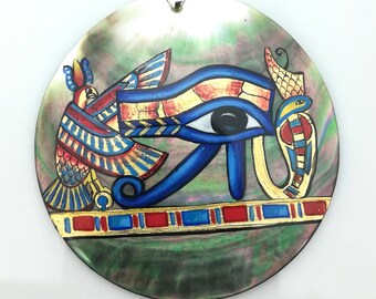 May include: A round, iridescent, mother-of-pearl pendant featuring a painted image of the Eye of Horus, a winged bird, and a snake. The Eye of Horus is blue with a black pupil, and the bird and snake are painted in red, yellow, and blue.