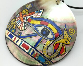 May include: A round, iridescent, mother-of-pearl pendant featuring a hand-painted depiction of the Eye of Horus, a cobra, and a bird. The pendant is painted in shades of blue, yellow, red, and gold.