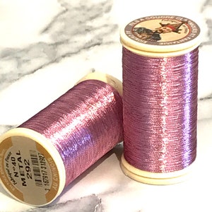 May include: Two spools of metallic pink thread, labeled "N°40 METAL 292" and "FLS A COUDRE CLASSIQUES AU CHINOIS".