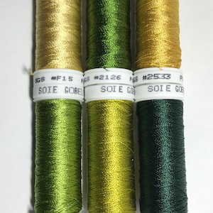 May include: Four spools of embroidery floss in shades of green and gold. The spools are labelled with the brand "SOIE GOBELIN" and the colour numbers #F15, #2126, #2533, #2124, #0199, and #50255.