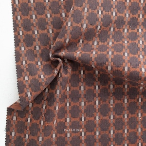 May include: Close-up of a brown fabric with an orange and white grid pattern. The fabric is folded, showing texture and depth. The word "FABLEISM" is printed in white at the bottom right corner.