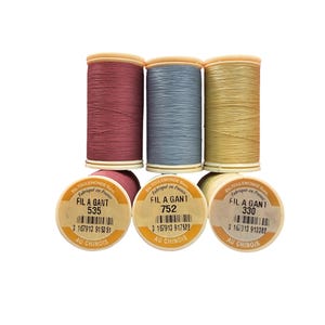 May include: Three spools of Fil Au Chinois Fil A Gant sewing thread in dusty rose, slate blue, and pale yellow. Each spool features a label with the text Ets Toulemonde Succ, Fabriqué en France, Fil A Gant, and a unique barcode and number.