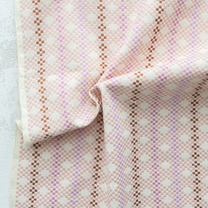May include: A close-up of a pink and brown woven fabric with a checkered pattern. The fabric is folded and has a soft, textured feel.