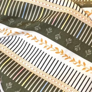 May include: Green and white striped fabric with a repeating pattern of small leaves and thin lines. The fabric has a subtle sheen and a soft texture.