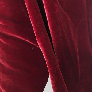 May include: Close-up of a deep red velvet fabric with a smooth, soft texture. The fabric is folded and draped, creating a luxurious and elegant look.