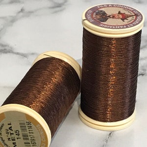 May include: Two spools of brown metallic thread with gold shimmer. The spools are labeled "Metal 145" and "Au Chinois".
