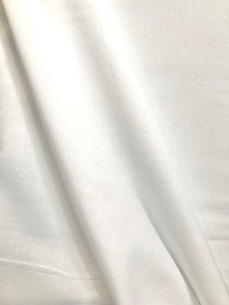 May include: White fabric with a smooth, silky texture. The fabric is folded and draped, creating soft folds and curves.