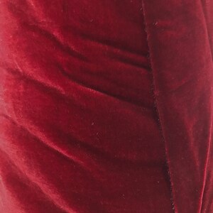 May include: Close-up of a deep red velvet fabric with a smooth, soft texture. The fabric is folded and has a subtle sheen.