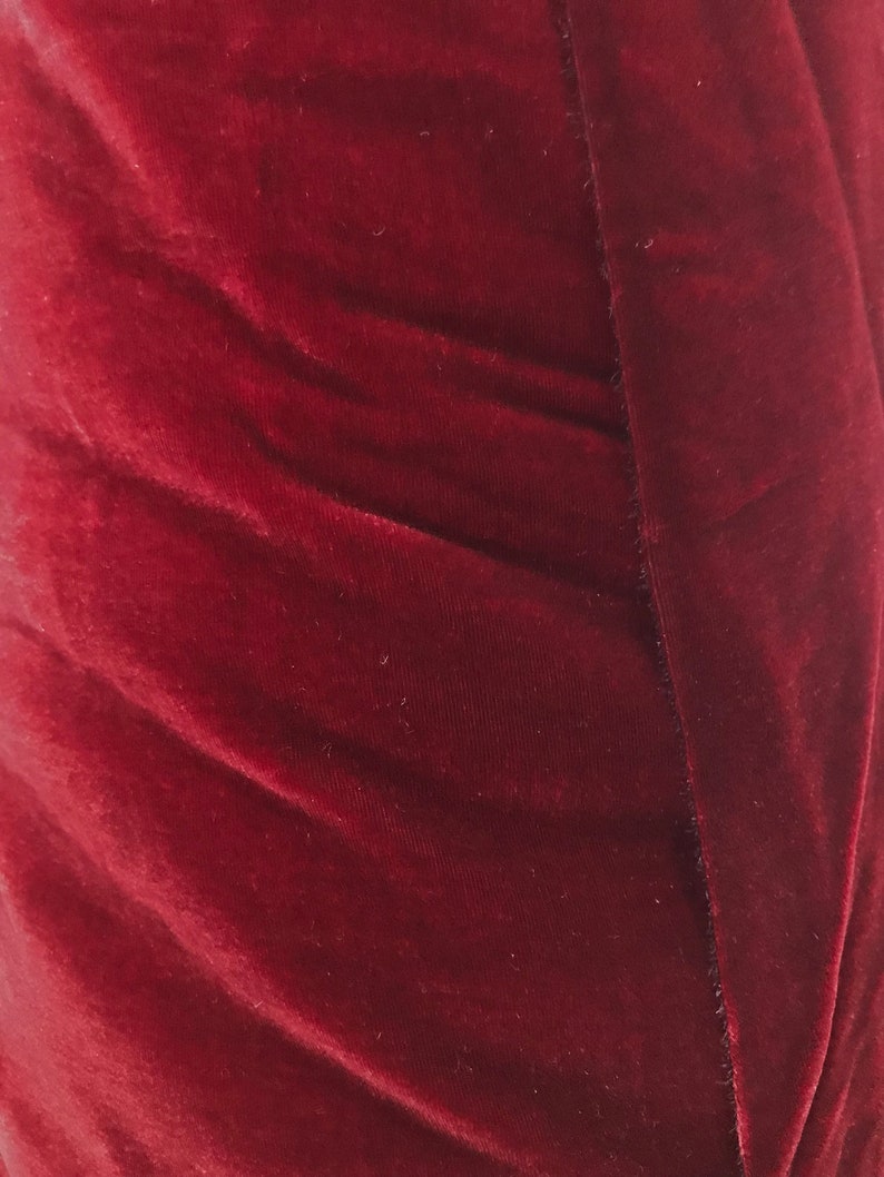May include: Close-up of a deep red velvet fabric with a smooth, soft texture. The fabric is folded and has a subtle sheen.