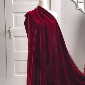 May include: A deep red velvet fabric draped over a mannequin. The fabric is soft and luxurious, with a rich, velvety texture.