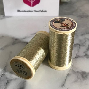 May include: Two spools of gold metallic thread. The spools are labeled "N°40 METAL 102" and "CLASIQUES ET FANTAISIE FILS A COUDRE AU CHINOIS".