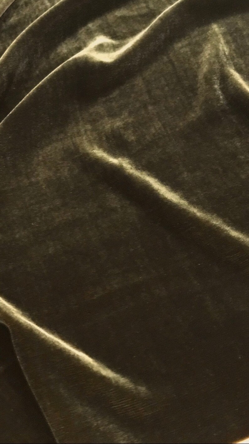May include: Close-up of olive green velvet fabric with soft folds and highlights. The plush material has a subtle sheen, creating a luxurious texture. Ideal for apparel, upholstery, or craft projects.