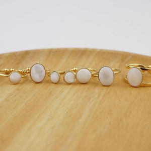 May include: Set of five gold rings with white oval stones. The rings are arranged on a wooden surface.