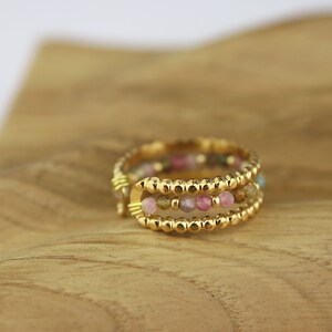 May include: A gold ring with three bands of small, colourful beads. The beads are pink, green, and brown.
