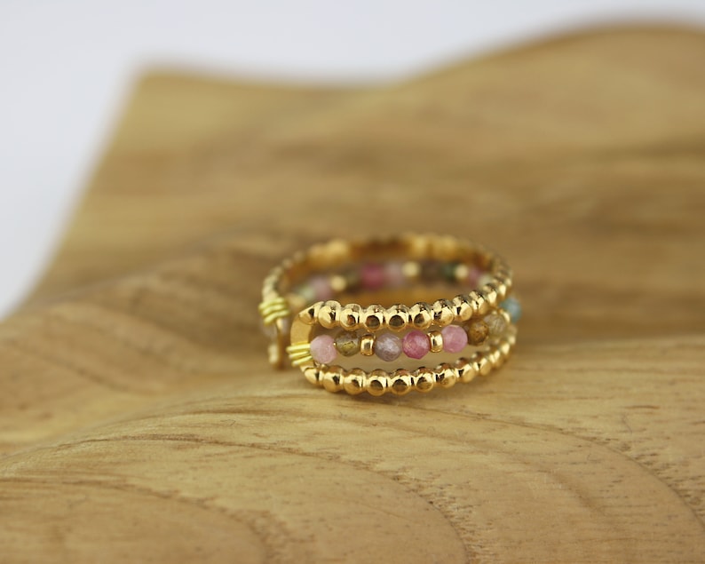 May include: A gold ring with three bands of small, colourful beads. The beads are pink, green, and brown.