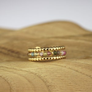 May include: A gold ring with three bands of small, colourful beads. The beads are a mix of pink, green, and yellow.