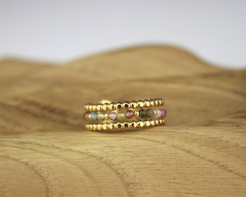May include: A gold ring with three bands of small, colourful beads. The beads are a mix of pink, green, and yellow.