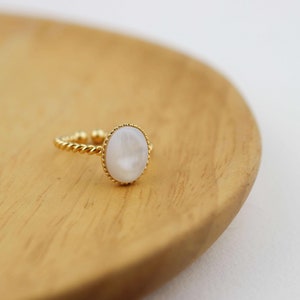 May include: A gold ring with a white oval-shaped stone set in a twisted band.