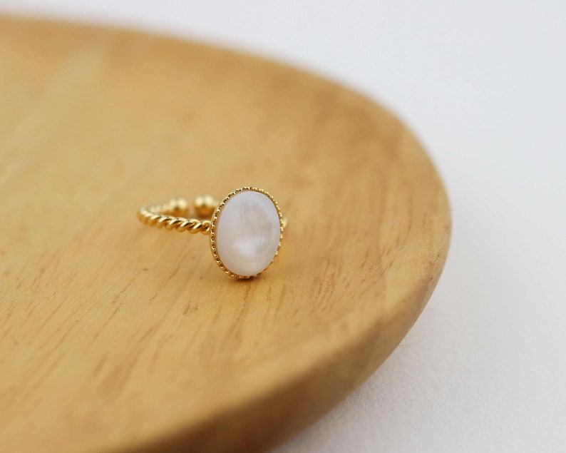 May include: A gold ring with a white oval-shaped stone set in a twisted band.