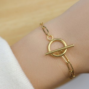 Peut inclure: Un bracelet en chaîne dorée avec un fermoir à glissière. La chaîne est composée de petits maillons ovales.