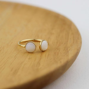 May include: A gold ring with two white oval stones set in a gold bezel. The ring is open on one side and has a delicate, beaded edge.