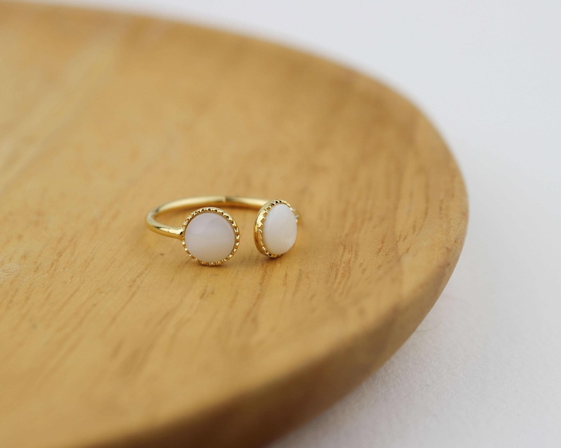 May include: A gold ring with two white oval stones set in a gold bezel. The ring is open on one side and has a delicate, beaded edge.