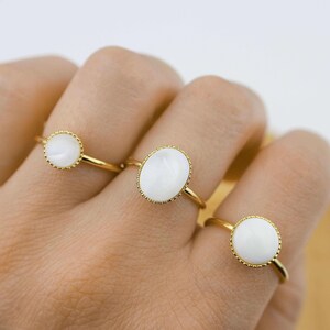 May include: Three gold rings with white oval-shaped stones. The stones are set in a gold bezel with a beaded edge.