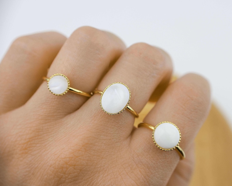 May include: Three gold rings with white oval-shaped stones. The stones are set in a gold bezel with a beaded edge.