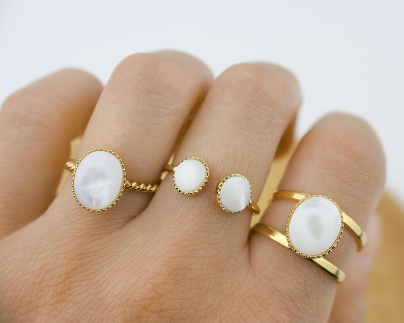 May include: Four gold rings with white oval-shaped stones. The rings are worn on a hand.