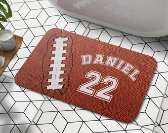 Pode incluir: Um tapete de banho castanho e branco com um design de bola de futebol. O tapete tem uma costura branca cosida no centro e o nome "DANIEL" e o número "22" em branco.