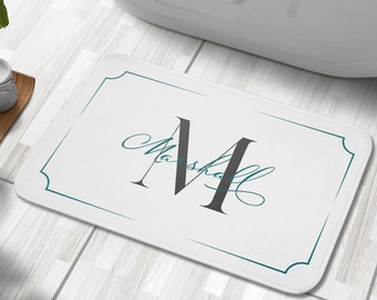 Puede incluir: Alfombra de baño blanca con borde turquesa y una gran letra "M" estilizada en gris con el nombre "Marshall" escrito en cursiva debajo.