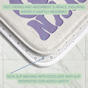 Pode incluir: Um tapete de banho branco com um gr&aacute;fico roxo que diz "M&atilde;e". O tapete tem um suporte antiderrapante e uma superf&iacute;cie absorvente de secagem r&aacute;pida.