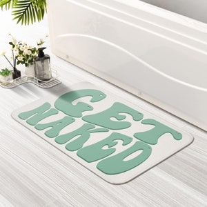 Pode incluir: Um tapete de banho branco com as palavras "GET NAKED" em letras estilizadas verdes.