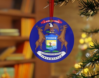 Puede incluir: Un adorno navideño redondo azul y blanco con el sello del estado de Michigan. El sello representa un águila calva con las alas extendidas, dos alces y una salida del sol sobre una masa de agua. El texto "TUEBOR" se muestra en el centro del sello, y el texto "E PLURIBUS UNUM" y "SI QUAERIS PENINSULAM AMOENAM CIRCUMSPICE" se muestra alrededor del sello.