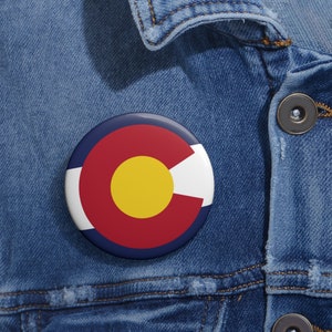 May include: A blue, red, yellow, and white button with the Colorado state flag design.