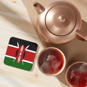 May include: A wooden coaster with the Kenyan flag printed on it. The coaster is next to a copper teapot and two cups of tea.