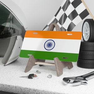 Peut inclure: Une plaque d'immatriculation en métal représentant le drapeau indien. Le drapeau est vert, blanc et orange avec une roue bleue au centre. La plaque d'immatriculation est sur un support en bois et il y a divers outils et un drapeau à damier en arrière-plan.