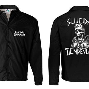 Könnte beinhalten: Schwarze Coach-Jacke mit weißem "Suicidal Tendencies"-Text auf der Vorder- und Rückseite. Auf der Rückseite befindet sich eine Totenkopf-Grafik mit dem Namen der Band. Die Jacke hat eine Knopfleiste und lange Ärmel.