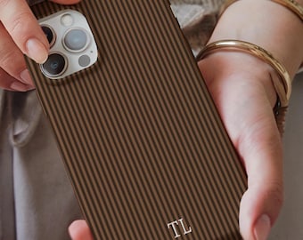 Könnte beinhalten: Braune und schwarz gestreifte Handyhülle mit den Initialen "TL" in Weiß. Die Hülle hat ein vertikales Streifenmuster und wird von einer Person in den Händen gehalten. Die Handyhülle ist für ein Smartphone konzipiert.