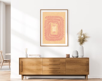 Könnte beinhalten: Ein gerahmter Druck mit einem pfirsichfarbenen Hintergrund und einem rosafarbenen Blumendesign. Das Design ist ein quadratischer Rahmen aus sich wiederholenden Blumenformen. Der Druck hängt an einer weißen Wand über einer Kommode aus Holz.