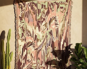 Op de afbeelding: Een geweven sprei met een kleurrijk abstract ontwerp. De sprei heeft een patroon van verticale en gebogen lijnen in tinten roze, groen, bruin en paars. De randen zijn afgewerkt met een franje.