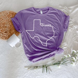 May include: Purple t-shirt with a white outline of the state of Texas and the word "Texans" written inside the outline.